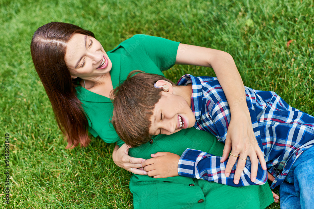 A mother and her hearing impaired son enjoy playful laughter in a vibrant green field. A mother and her hearing impaired son enjoy playful laughter in a vibrant green field.