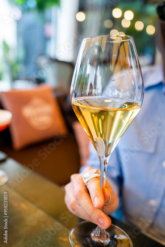 A close-up of a person’s hand holding a glass of white wine, with a blurred background suggesting a cozy restaurant setting. The image captures a moment of relaxation and enjoyment