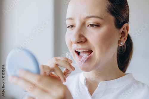 Woman Is Putting On A Transparent Aligner While Looking In A Small Mirror. Dental Health Medical Care Concept. photo