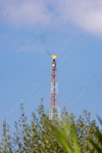 Tall industrial gas flare stack burning a bright flame against a blue sky in the north of Algeria.