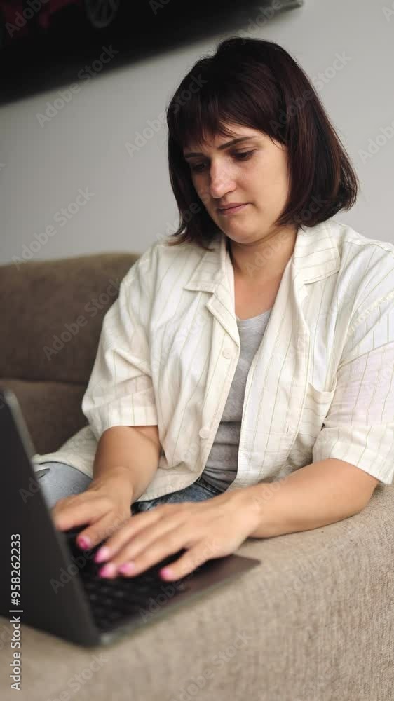 Nice brunette woman works remotely from a computer, laptop, remote work, online, work from home, technology, typing on a keyboard, searching the Internet, girl sitting on the couch, comfort, vertical Nice brunette woman works remotely from a computer, laptop, remote work, online, work from home, technology, typing on a keyboard, searching the Internet, girl sitting on the couch, comfort, vertical