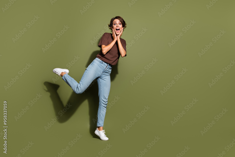 Full length photo of overjoyed astonished girl wear oversize t-shirt denim pants palms on cheek staring isolated on green color background Full length photo of overjoyed astonished girl wear oversize t-shirt denim pants palms on cheek staring isolated on green color background