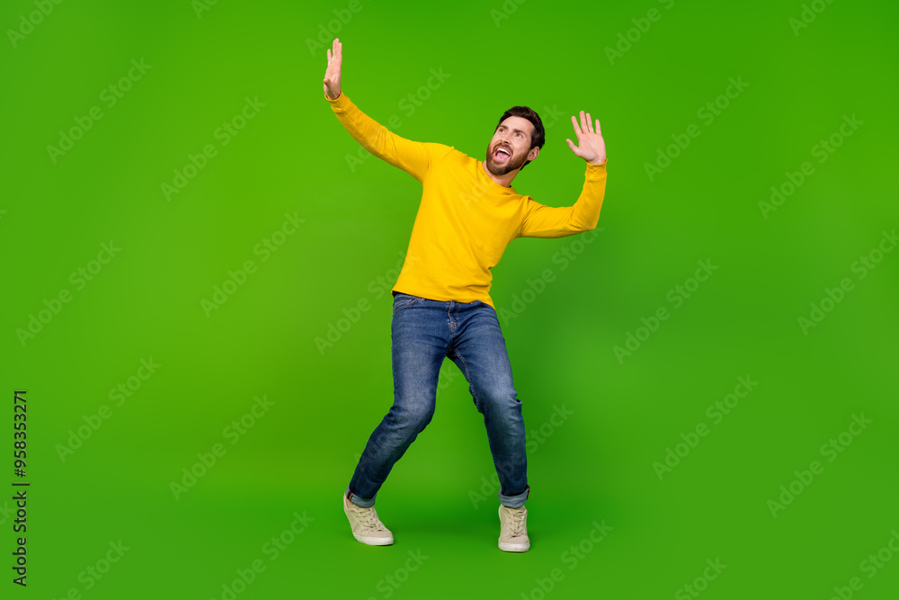 Full length photo of handsome young guy dance have fun look empty space dressed stylish yellow garment isolated on green color background Full length photo of handsome young guy dance have fun look empty space dressed stylish yellow garment isolated on green color background