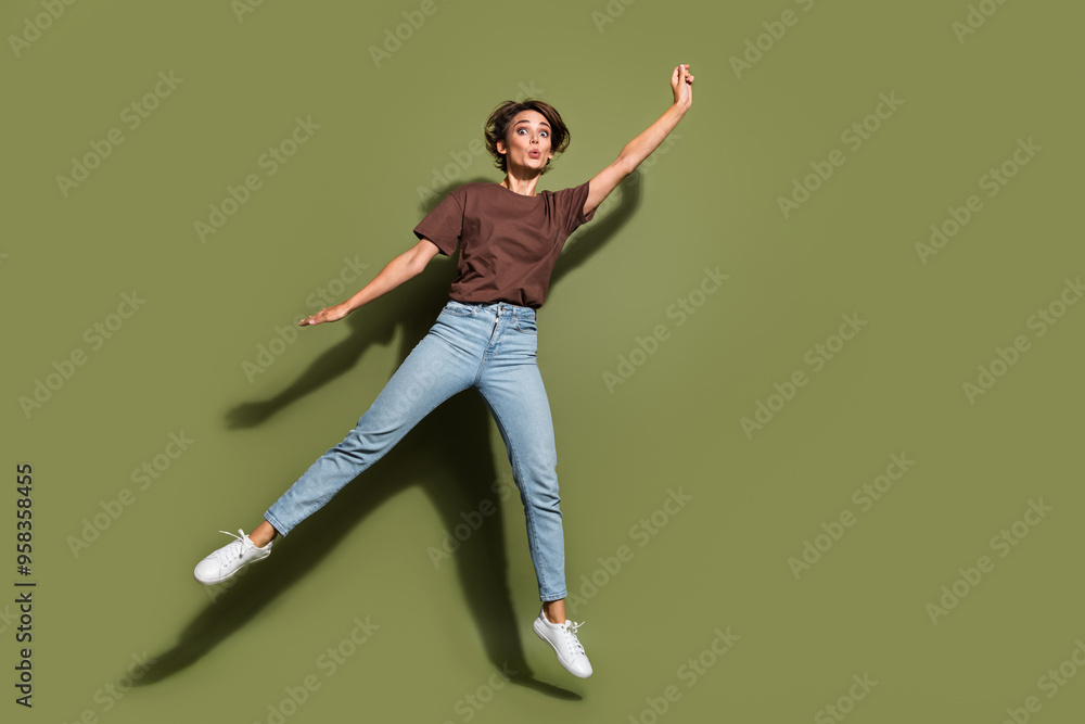 Full size photo of optimistic astonished woman dressed brown t-shirt denim pants flying raising palm up isolated on khaki color background Full size photo of optimistic astonished woman dressed brown t-shirt denim pants flying raising palm up isolated on khaki color background