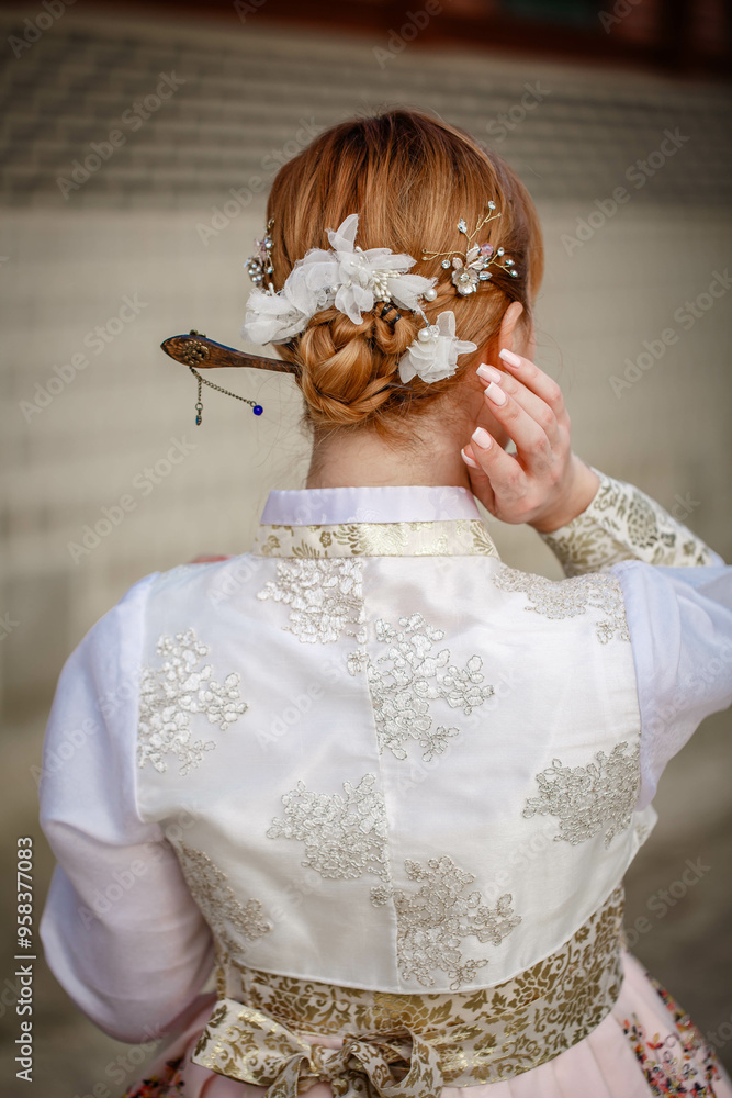 Picture of traditional Korean hairstyle for festive occasions. A girl dressed in a classic ethnic dress standing outdoor, view from the back.