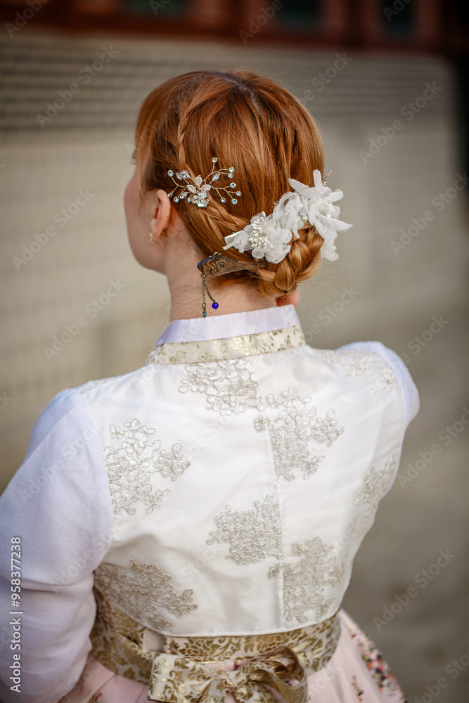 Picture of traditional Korean hairstyle for festive occasions. A girl dressed in a classic ethnic dress standing outdoor, view from the back.