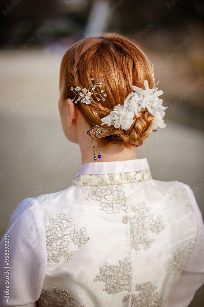 Picture of traditional Korean hairstyle for festive occasions. A girl dressed in a classic ethnic dress standing outdoor, view from the back.