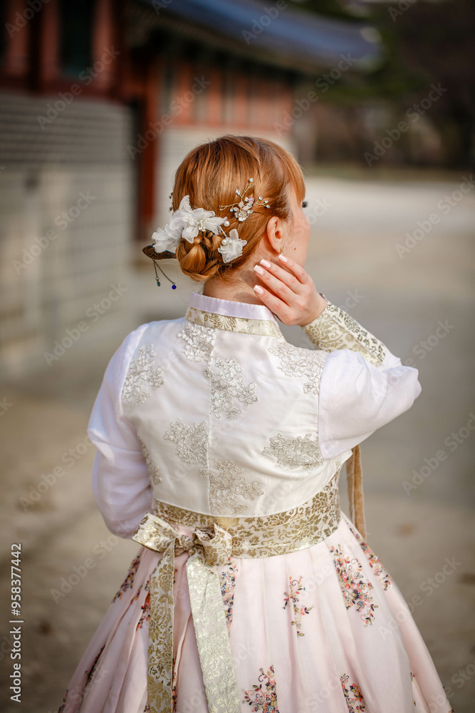 Picture of traditional Korean hairstyle for festive occasions. A girl dressed in a classic ethnic dress standing outdoor, view from the back.