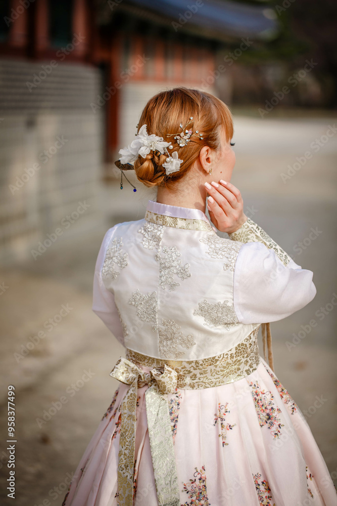 Picture of traditional Korean hairstyle for festive occasions. A girl dressed in a classic ethnic dress standing outdoor, view from the back.