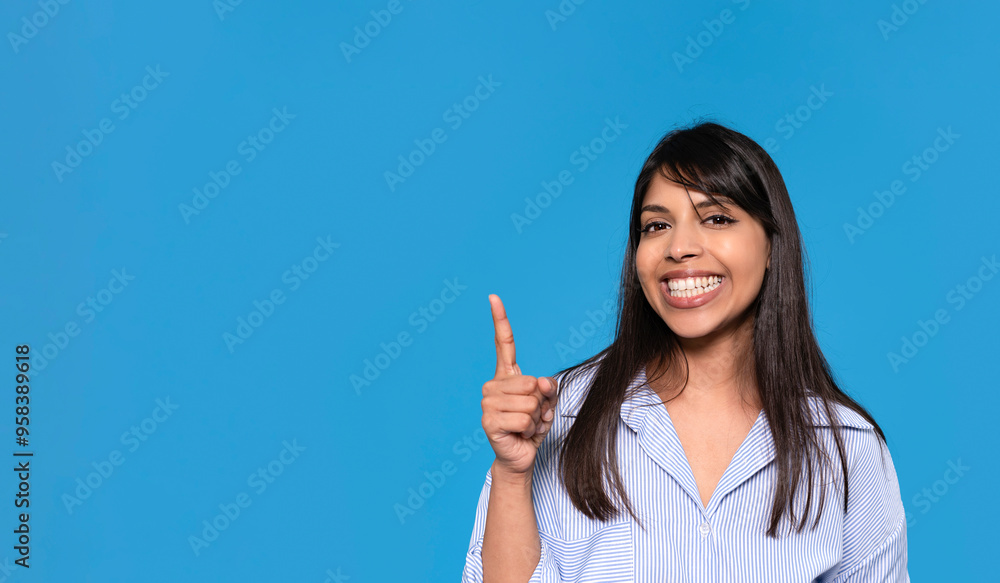 Joyful Woman With a Beaming Smile Gestures Cheerfully Against a Vibrant Blue Backdrop Joyful Woman With a Beaming Smile Gestures Cheerfully Against a Vibrant Blue Backdrop