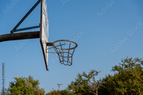 A basketball net is hanging from a metal pole. The net is empty and the sky is clear