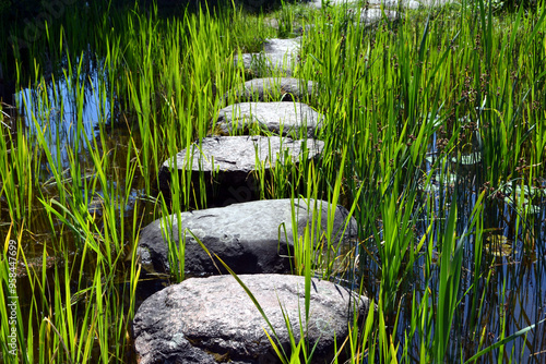 Small stony footbridge, stone bridge over the stream or little pond. Pathway through the stream