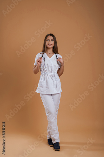In doctor coat, with stethoscope. Young pretty woman is against background in the studio