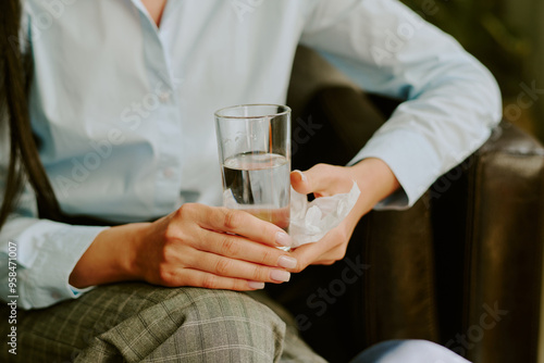 Close-up of a person holding a glass of water and a napkin while sitting on a sofa in relaxed posture