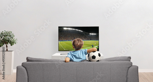 Rear view shot of a boy holding a football and watching a match on tv photo