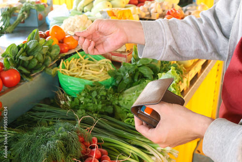 image of a man's hand buying greens and vegetables at a market. The market is filled with onions, radishes, cilantro, basil, dill, parsley