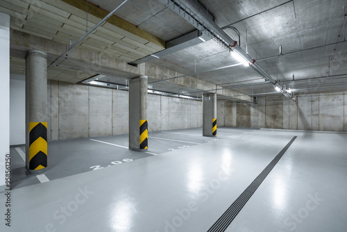 An empty underground parking garage with concrete walls, floors, and columns, yellow and black safety markings, bright overhead lighting, and clearly numbered parking spaces. photo