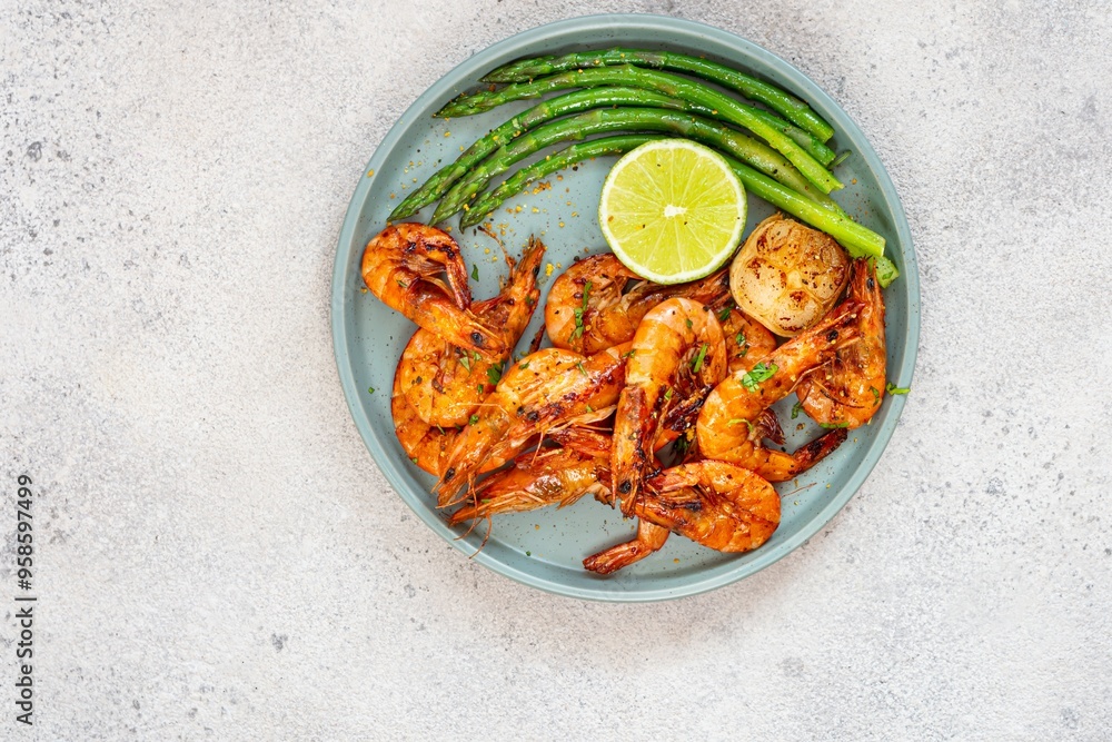 Grilled shrimp (tiger prawns) in spices with asparagus and a slice of lime (lemon) on a plate on a light background. Grilled shrimp (tiger prawns) in spices with asparagus and a slice of lime (lemon) on a plate on a light background.