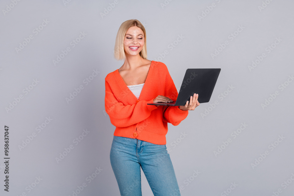 Photo of pretty young girl use laptop orange cardigan isolated on grey color background Photo of pretty young girl use laptop orange cardigan isolated on grey color background