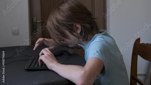 Young man is sitting at a table typing on a keyboard, he is hunched over and developing bad posture