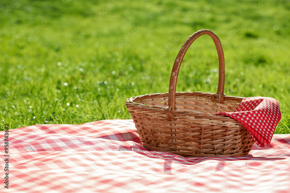One picnic wicker basket with checkered napkin and blanket on green grass. Space for text One picnic wicker basket with checkered napkin and blanket on green grass. Space for text