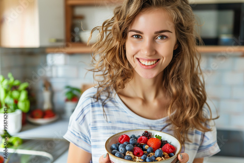Young woman holding a bowl with granola and berries in the kitchen.