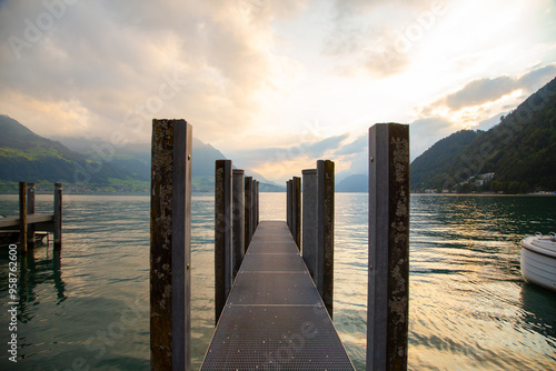 a pier with wooden pillars on a lake surrounded by mountains at sunset light. travel concept photo