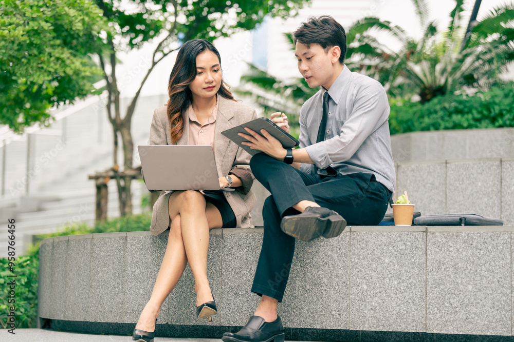 Obraz premium A male and female business team engage in discussion utilizing a laptop and notes. team sitting at outdoor pedestrian landscape. reflecting the importance of collaboration and strategic planning.