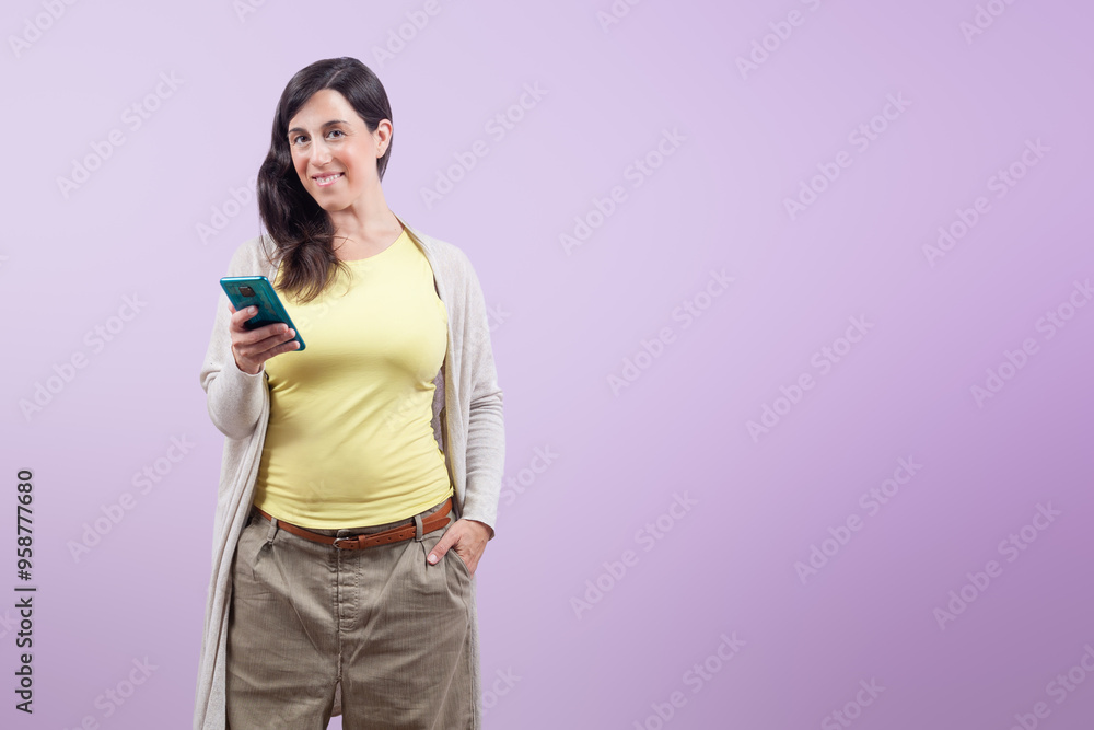A woman holds a mobile phone in her hand. She smiles and looks at the camera A woman holds a mobile phone in her hand. She smiles and looks at the camera