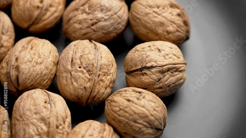 Freshly harvested walnuts gathered from the orchard on a black ceramic plate close up. Rotation