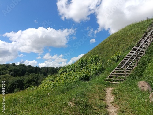 Bubiai hill during sunny day. Small hill. Grass is growing on hill. Staircase leading to the top. Sunny day with white and gray clouds in sky. Nature. Bubiu piliakalnis. photo