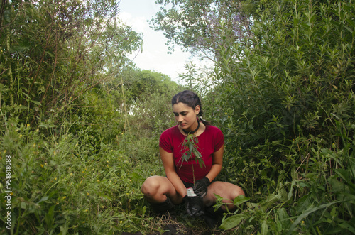 joven mujer plantando una planta de cannabis en un parque lleno de vegetación photo