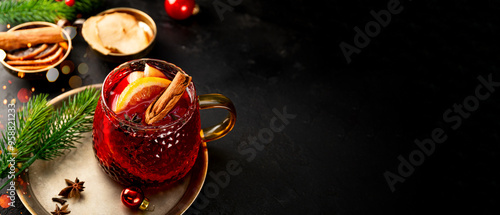 A glass mug of mulled wine on the black background and Christmas decorations. Festive winter drink, web banner with copy space for text
