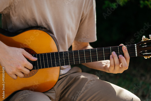 young man is playing acoustic guitar outside on summer