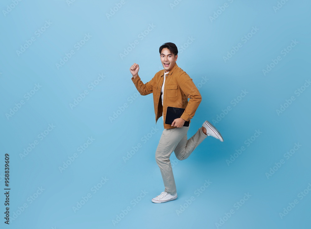 Full length Asian man holding tablet running with happy smile isolated on blue background. Happy man joyful run in copy space. Full length Asian man holding tablet running with happy smile isolated on blue background. Happy man joyful run in copy space.