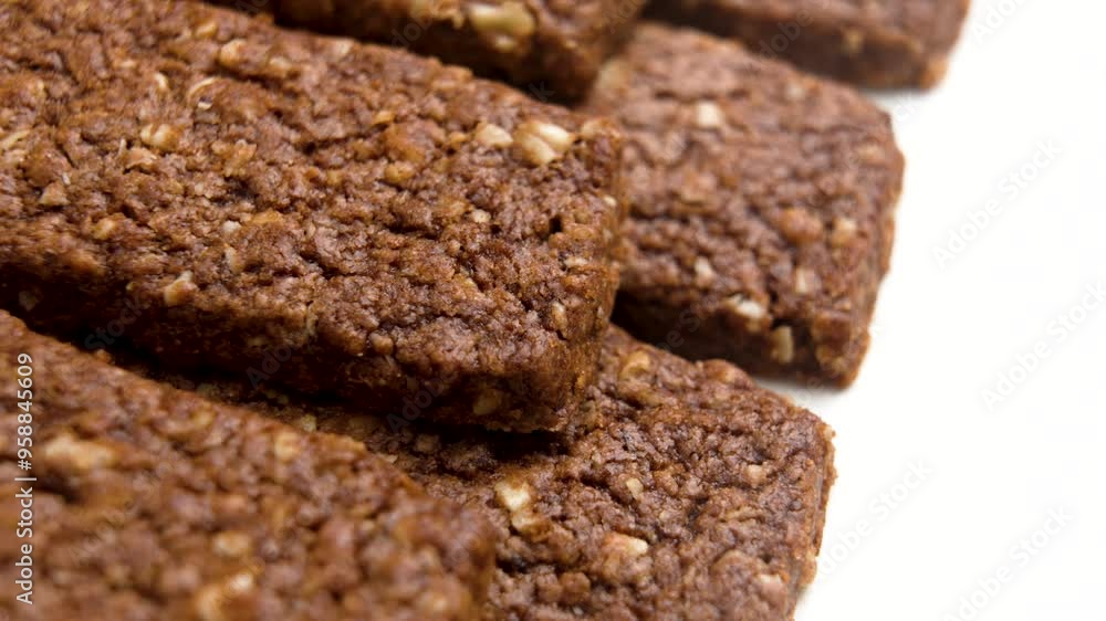 Nutritious chocolate energy bars filled with oats and nuts on a beige ceramic plate. Perfect for a healthy snack or an energy boost any time of day. Macro. Rotation Nutritious chocolate energy bars filled with oats and nuts on a beige ceramic plate. Perfect for a healthy snack or an energy boost any time of day. Macro. Rotation