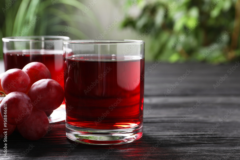 Tasty grape juice in glasses and berries on black wooden table against blurred green background, closeup. Space for text Tasty grape juice in glasses and berries on black wooden table against blurred green background, closeup. Space for text