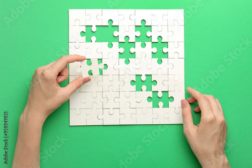 Tablou pe pânză Woman solving white puzzle on green background, closeup