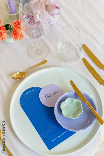 A stylish, modern  wedding place setting featuring a blue and lavender color scheme, modern dinnerware, and floral accents on a white tablecloth photo