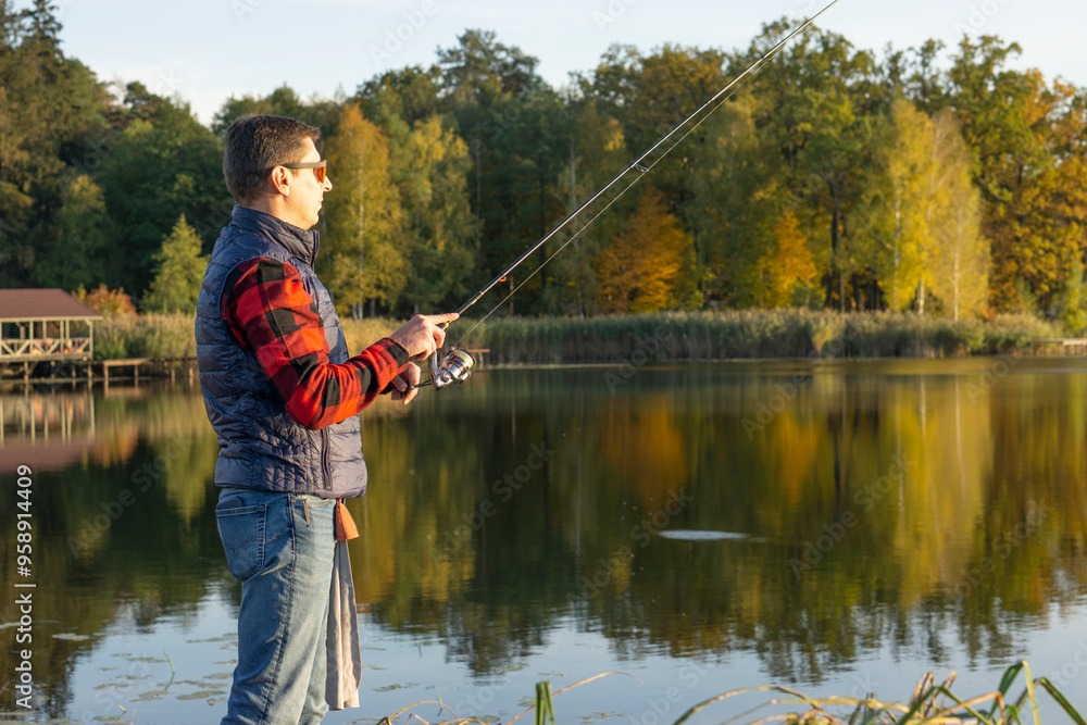 A man fishing by a calm lake with a fishing rod on a sunny autumn day, surrounded by nature, with copy space.
A man fishing by a calm lake with a fishing rod on a sunny autumn day, surrounded by nature, with copy space.