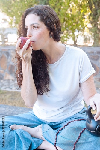 Woman Eating an Apple While Holding a Kettlebell Outdoors