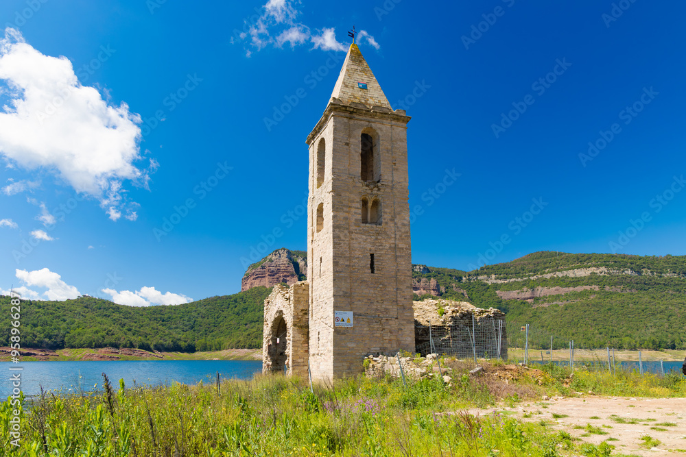La fotografía muestra la iglesia de Sant Romà de Sau en primer plano, destacando su campanario de piedra junto al embalse del Pantano de Sau, Cataluña, España La fotografía muestra la iglesia de Sant Romà de Sau en primer plano, destacando su campanario de piedra junto al embalse del Pantano de Sau, Cataluña, España