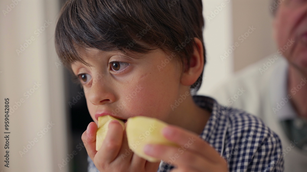 Young boy eating apple slice, close-up on face, thoughtful expression, family moment, enjoying healthy snack, home setting, innocent look focused child