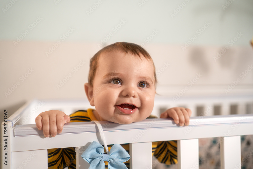 Smiling baby boy in a yellow striped outfit standing in his crib. Cheerful toddler enjoying his time in a bright and cozy nursery.. Smiling baby boy in a yellow striped outfit standing in his crib. Cheerful toddler enjoying his time in a bright and cozy nursery..