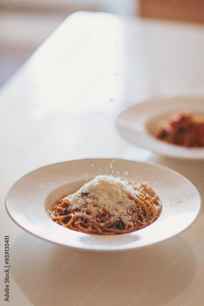 Scattering freshly grated parmesan over the pasta. Spaghetti with tomato sauce and basil on a plate. Hands grating Parmesan cheese on a spaghetti pasta. Traditional Italian food. Scattering freshly grated parmesan over the pasta. Spaghetti with tomato sauce and basil on a plate. Hands grating Parmesan cheese on a spaghetti pasta. Traditional Italian food.