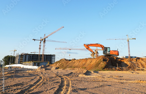 Construction site. Buildings under construction. Tower Cranes on Residential Buildings construction. Excavator on groundwork. Backhoe on roadworks. Excavator on earthworks for road construction.