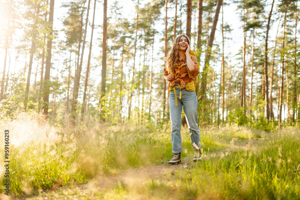 A young woman with curly hair enjoys a serene hike in a sunny forest during the late afternoon, carrying a yellow backpack on her shoulders. The concept of tourism, relaxation, youth and nature. A young woman with curly hair enjoys a serene hike in a sunny forest during the late afternoon, carrying a yellow backpack on her shoulders. The concept of tourism, relaxation, youth and nature.