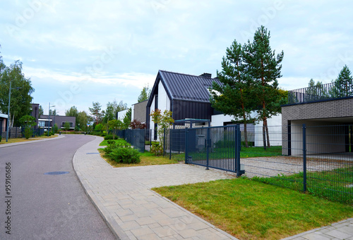 Prefab house. Street in residential area. Contemporary Residence in suburb. Rows of modern houses along road. Family house, Modern Home outside city. Trees, green lawn at Villa. Modern barnhouse.