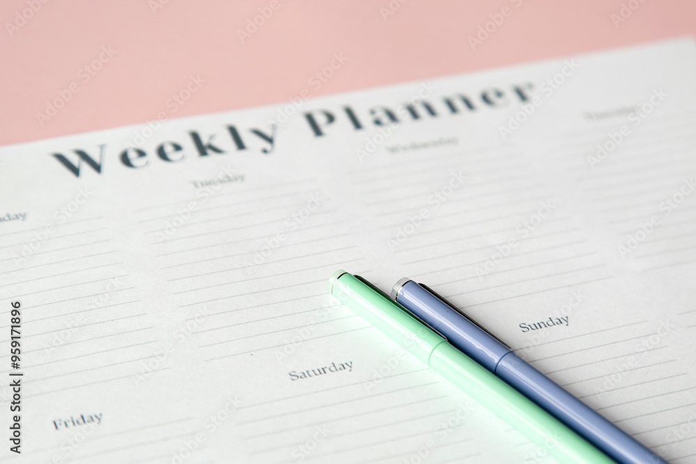 white weekly planner sheet on pink background and four colored pens, planning concept white weekly planner sheet on pink background and four colored pens, planning concept