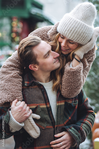Quadro su tela Beautiful young loving couple embracing, kissing, enjoying winter vacation, cold snowy day on a street city Christmas market outdoors